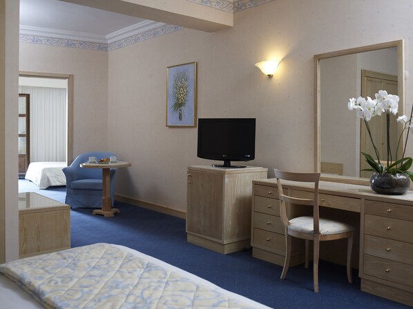 Une chambre d’hôtel avec un lit, un bureau avec un ordinateur, une chaise, une petite table avec une tasse et une assiette, un tableau au mur et un grand miroir.