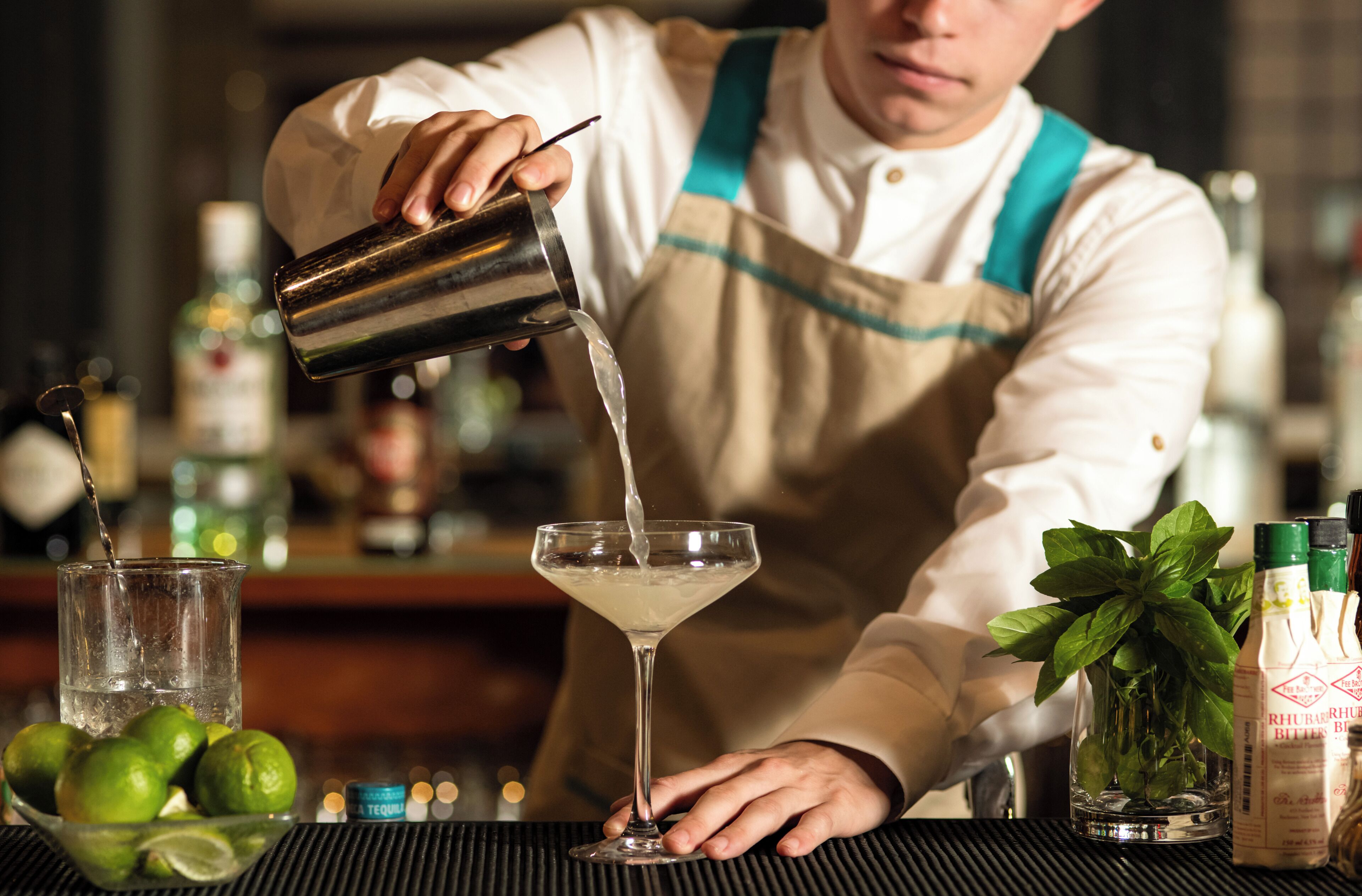 A bartender pouring a drink into a martini glass.
