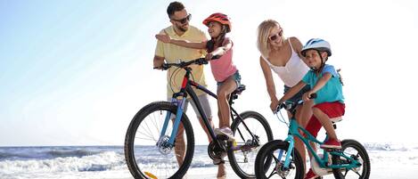 A group of people on bicycles at a beach with ocean in the background.