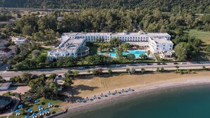 Eine Luftaufnahme eines Resorts mit einem großen Gebäude, einem Schwimmbad und einem Strandbereich mit Sonnenschirmen.
