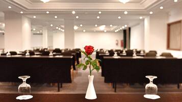Un salón de conferencias con mesas y sillas, un jarrón blanco con una rosa roja, y dos jarrones de vidrio vacíos sobre la mesa.