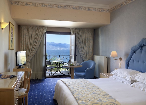 Habitación de hotel con cama, escritorio, silla, mesa con vistas al mar y balcón con cortinas.