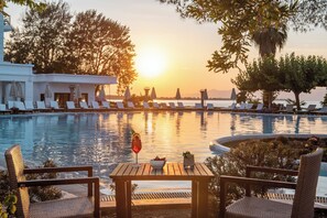 Un espace aménagé au bord de la piscine, avec des chaises longues et une table sur laquelle sont disposés des boissons et un saladier rempli de fruits.