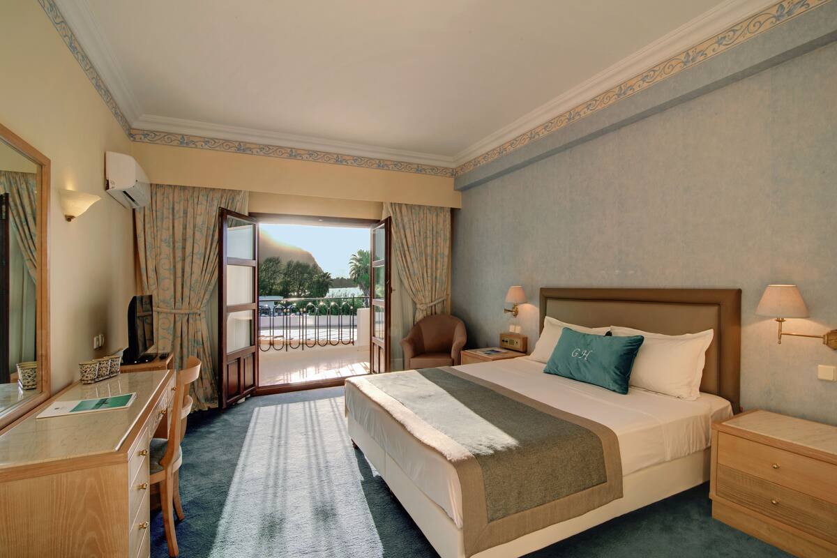 Ein Hotelzimmer mit einem großen Bett, einem Schreibtisch, einem Stuhl, einem Nachttisch und einem Fenster mit Vorhängen.
