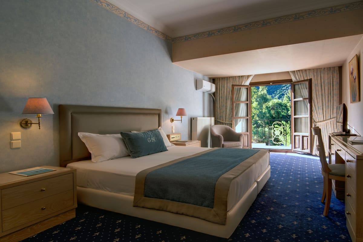 Ein Hotelzimmer mit einem großen Bett, einem Schreibtisch, einem Stuhl und Blick ins Freie.