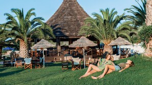 Ein Resort mit strohgedecktem Gebäude, Sitzgelegenheiten im Freien und Palmen.