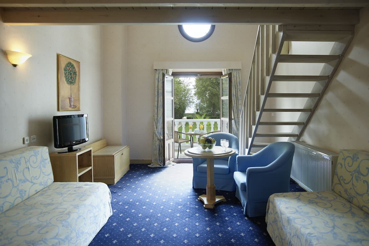 Ein Zimmer mit einem Bett, einem Fernseher, einem Tisch mit Stühlen, einem Balkon mit Geländer und einer Treppe.