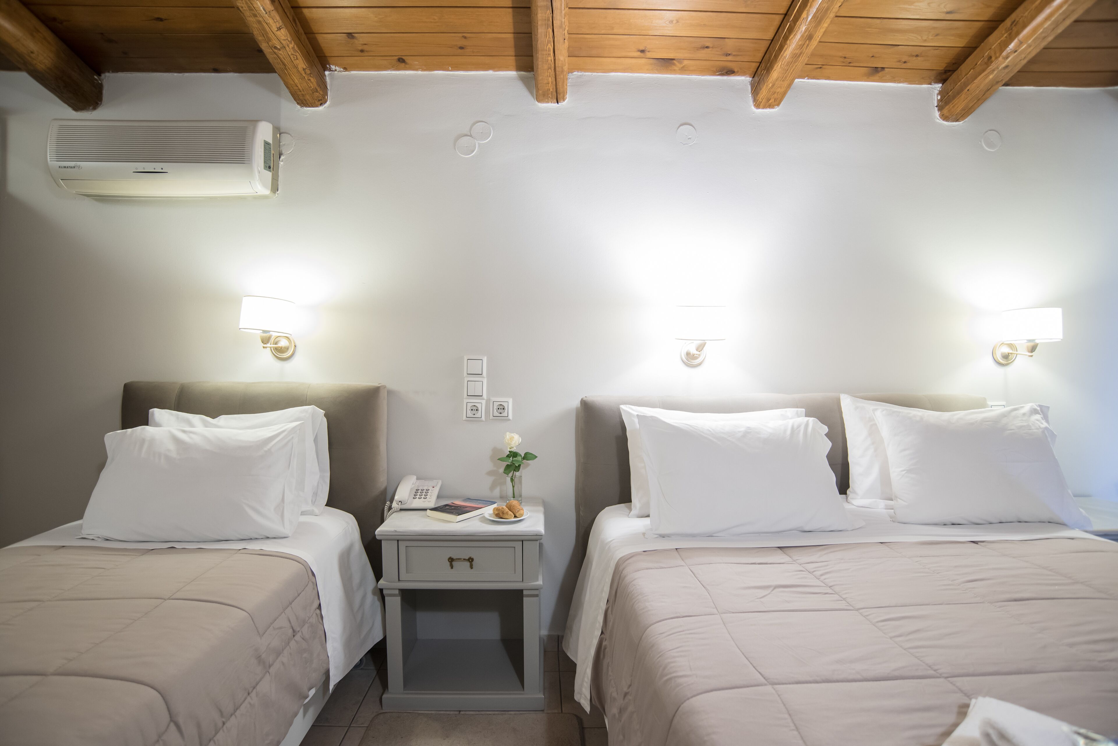 A hotel room with two beds, a nightstand with a phone and a book, and an air conditioner on the wall.
