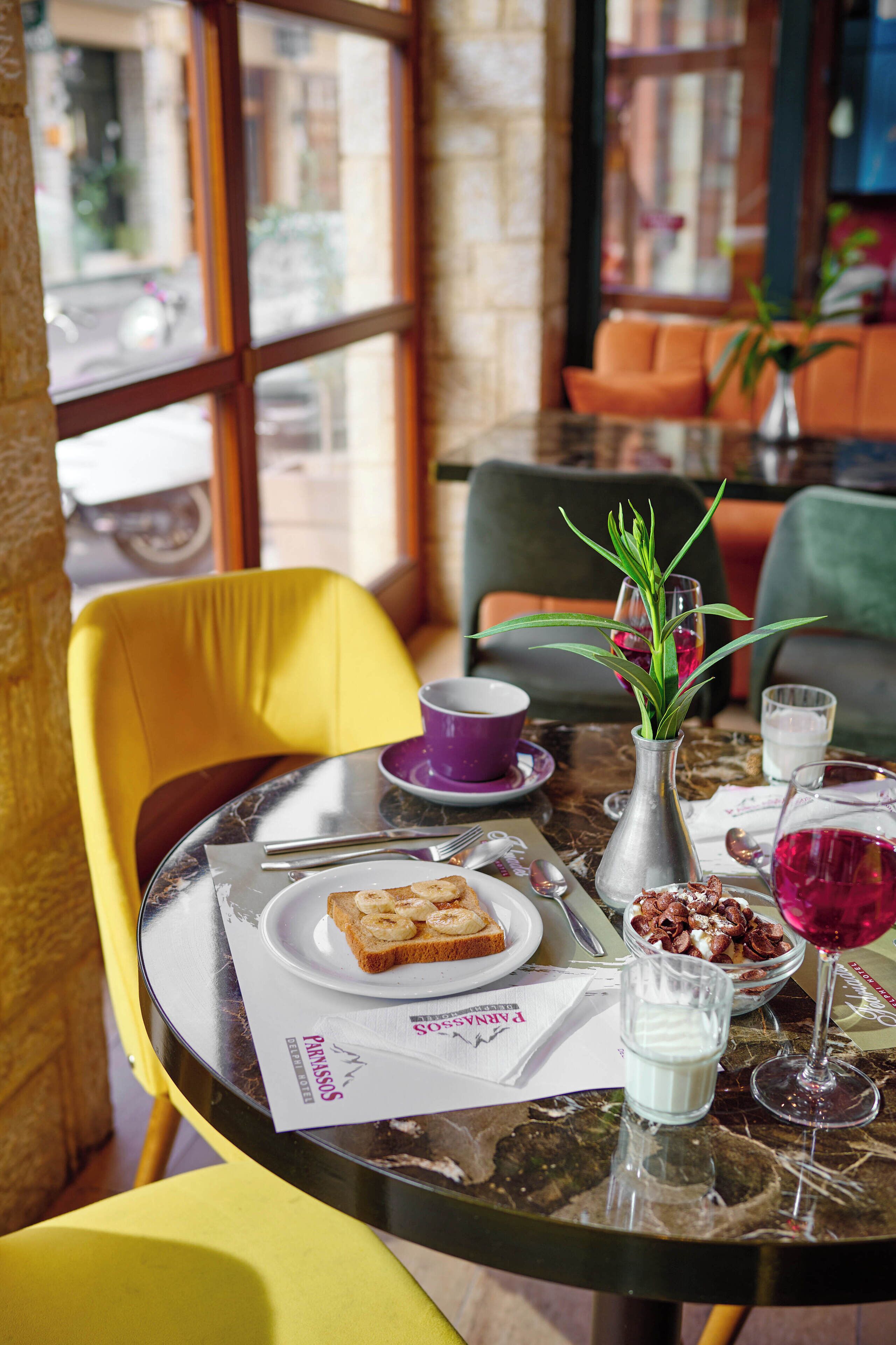 Une table à manger avec une assiette de nourriture, un vase contenant des plantes vertes et un verre de vin rouge.