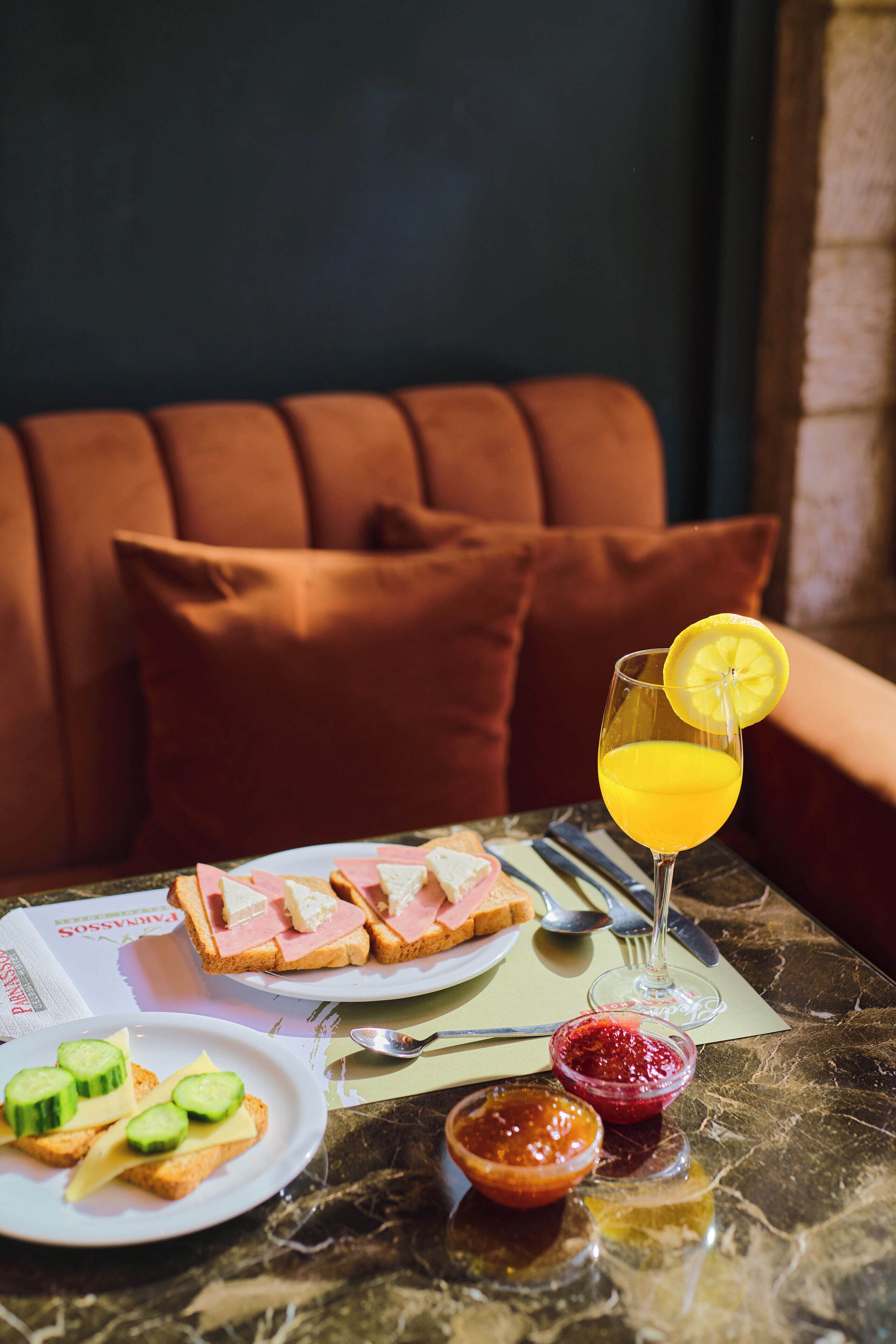 A dining table with a sandwich, a glass of orange juice, and two small bowls of jam.