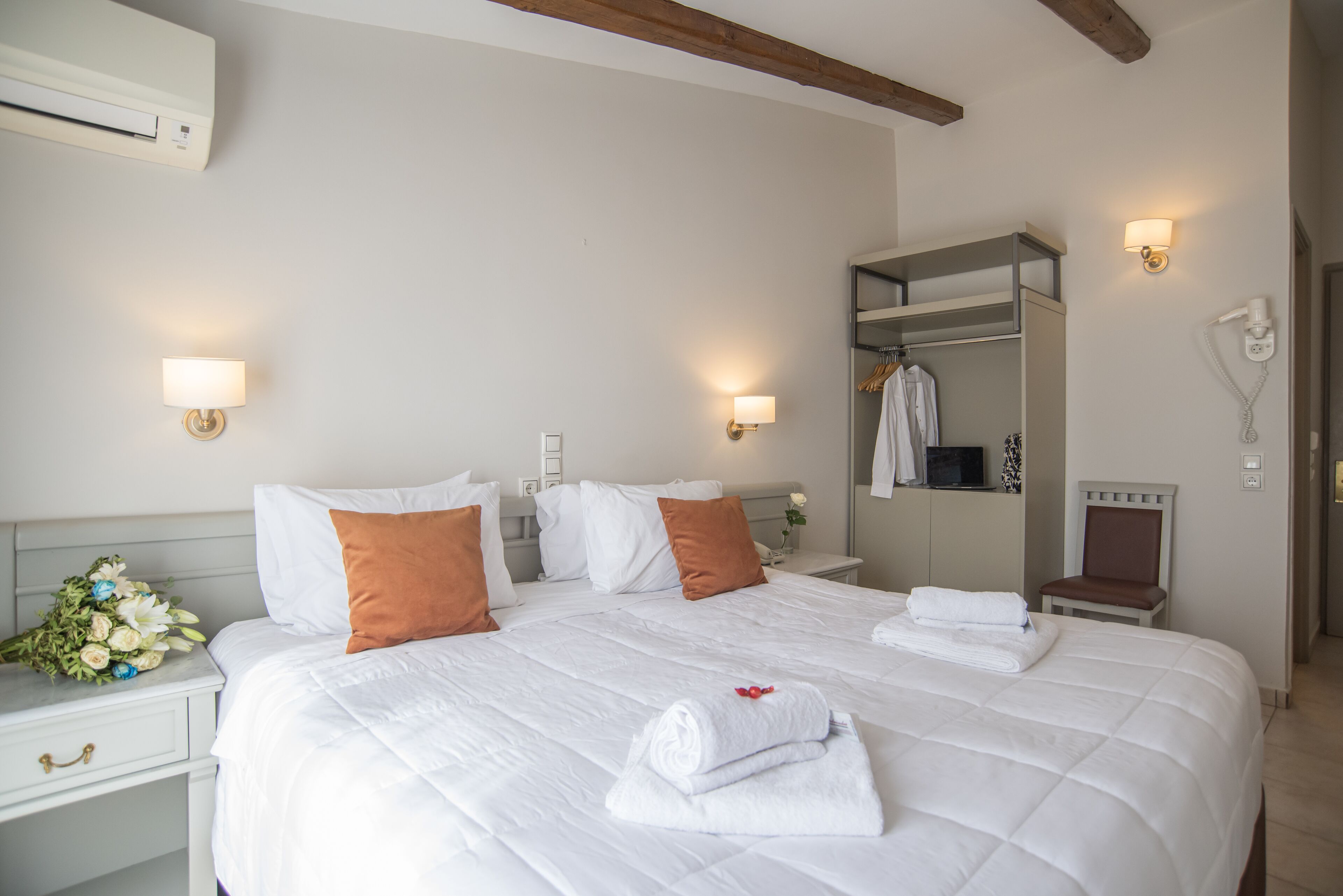 A hotel room with a large bed, white bedding, a nightstand with a lamp, a mirror, a robe, and a hairdryer.