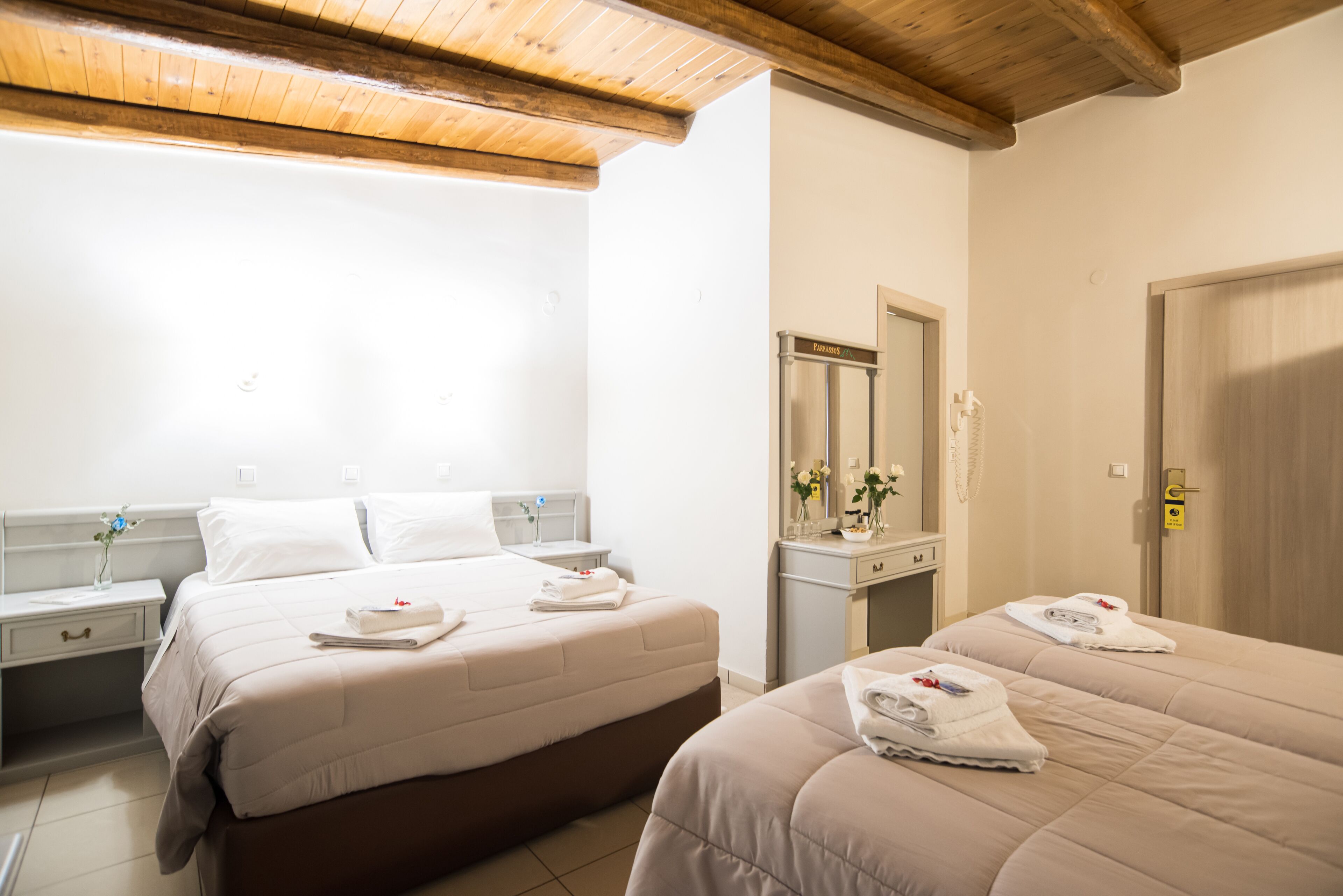 Habitación de hotel con dos camas, techo de madera, baño con espejo y una puerta con cerradura.