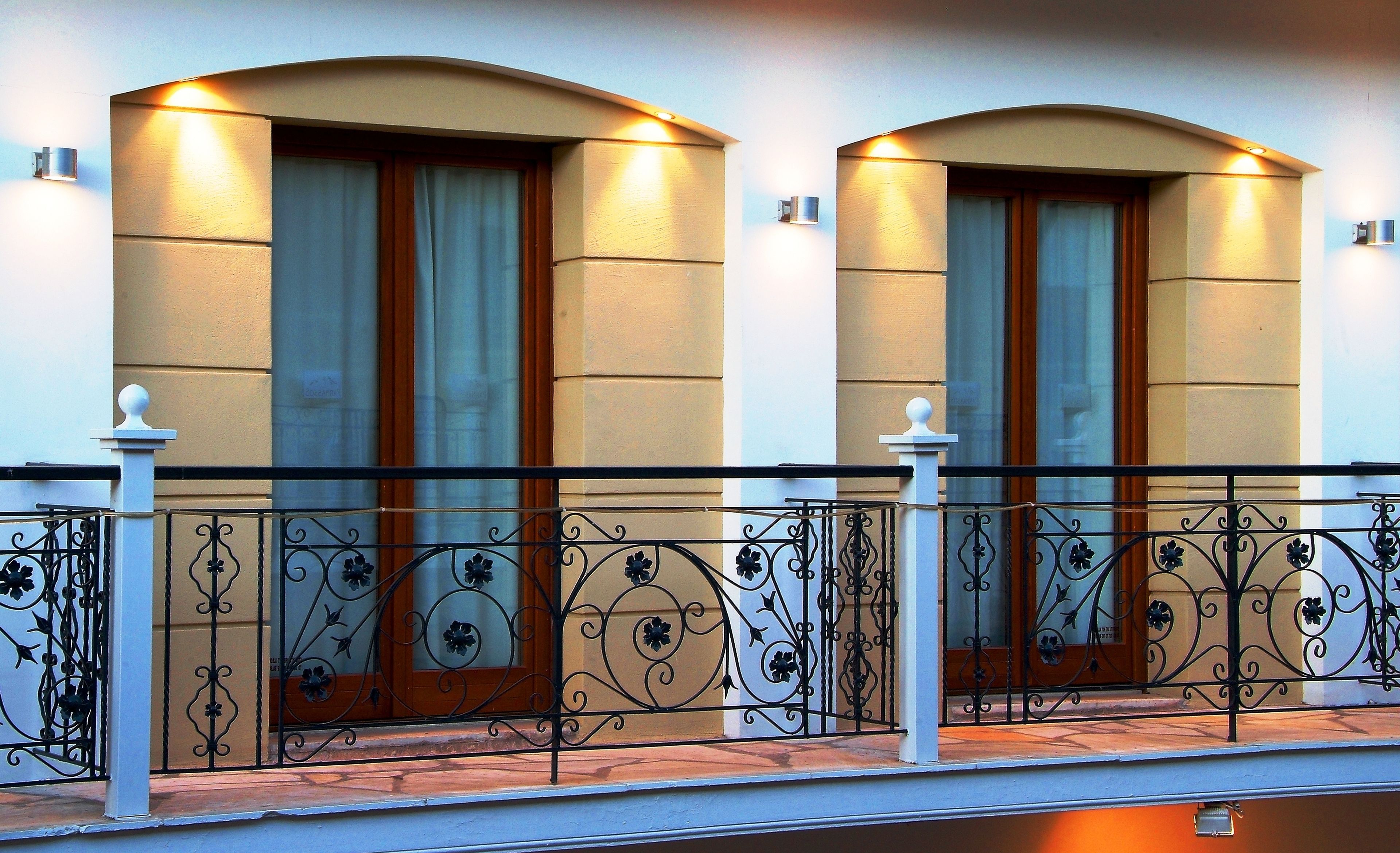 A building facade with two large windows, each with a wooden door and a white curtain.