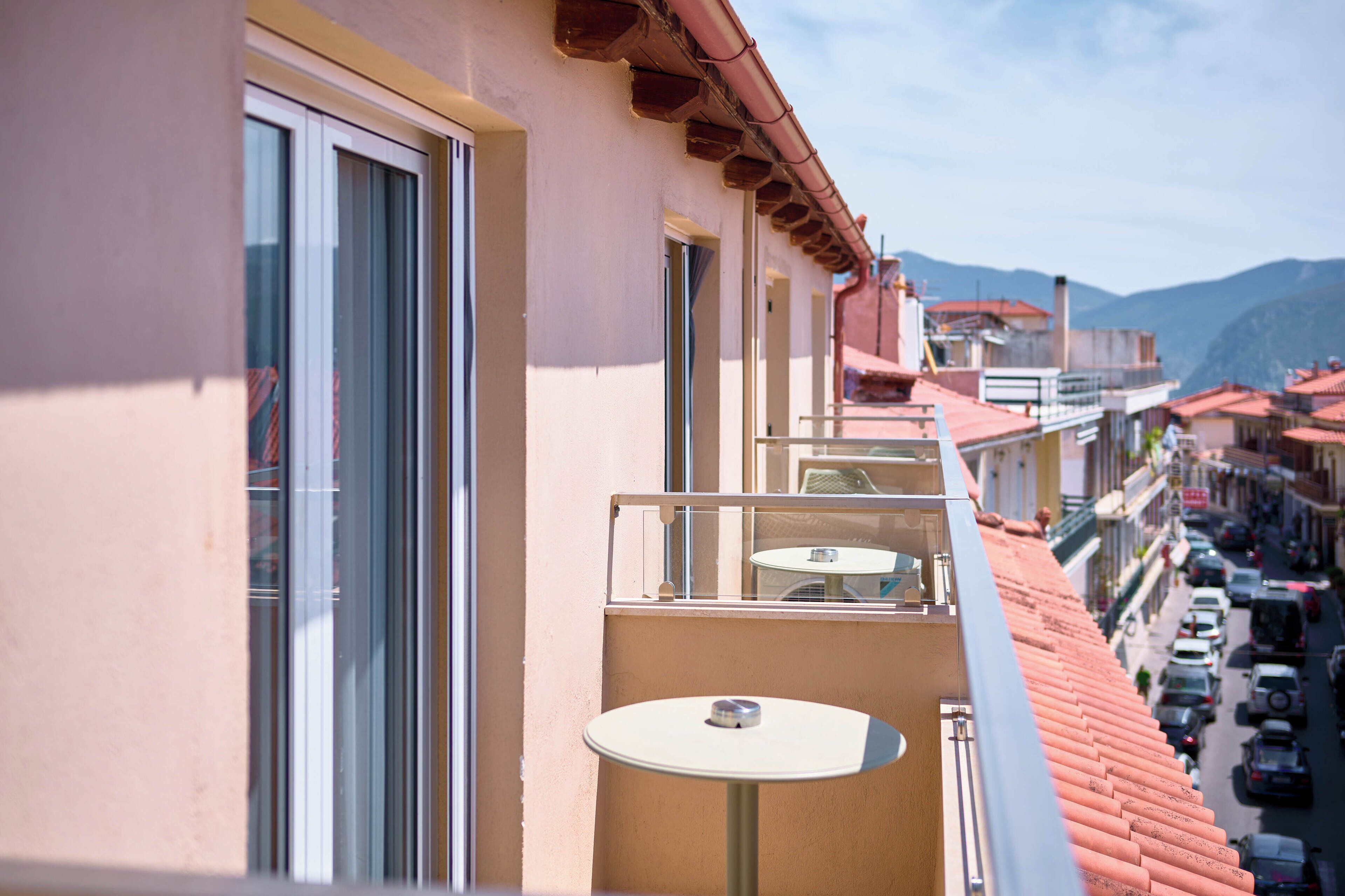 Un balcón con mesa y sillas, con vista a una calle con coches aparcados y edificios.