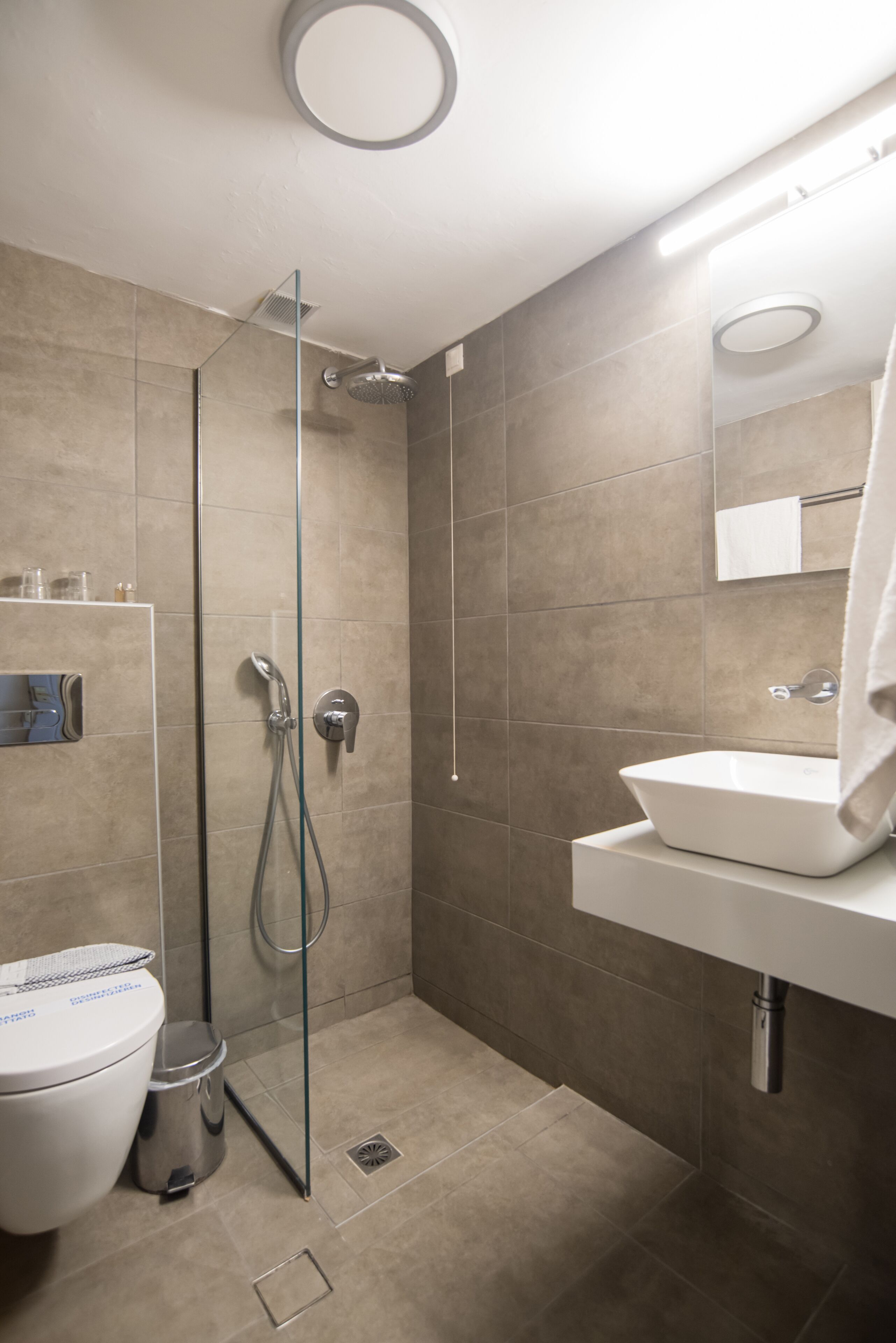 Een moderne badkamer met een glazen douchecabine, een witte wastafel en een toilet.