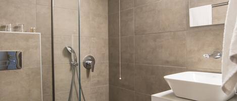 Een moderne badkamer met een glazen douchecabine, een witte wastafel en een toilet.