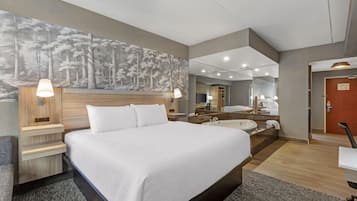 Habitación de hotel con una cama grande, una zona de estar con una silla, un escritorio, un espejo, una bañera y un mural grande en la pared.