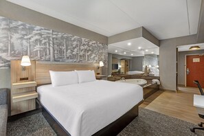 Habitación de hotel con una cama grande, una zona de estar con una silla, un escritorio, un espejo, una bañera y un mural grande en la pared.