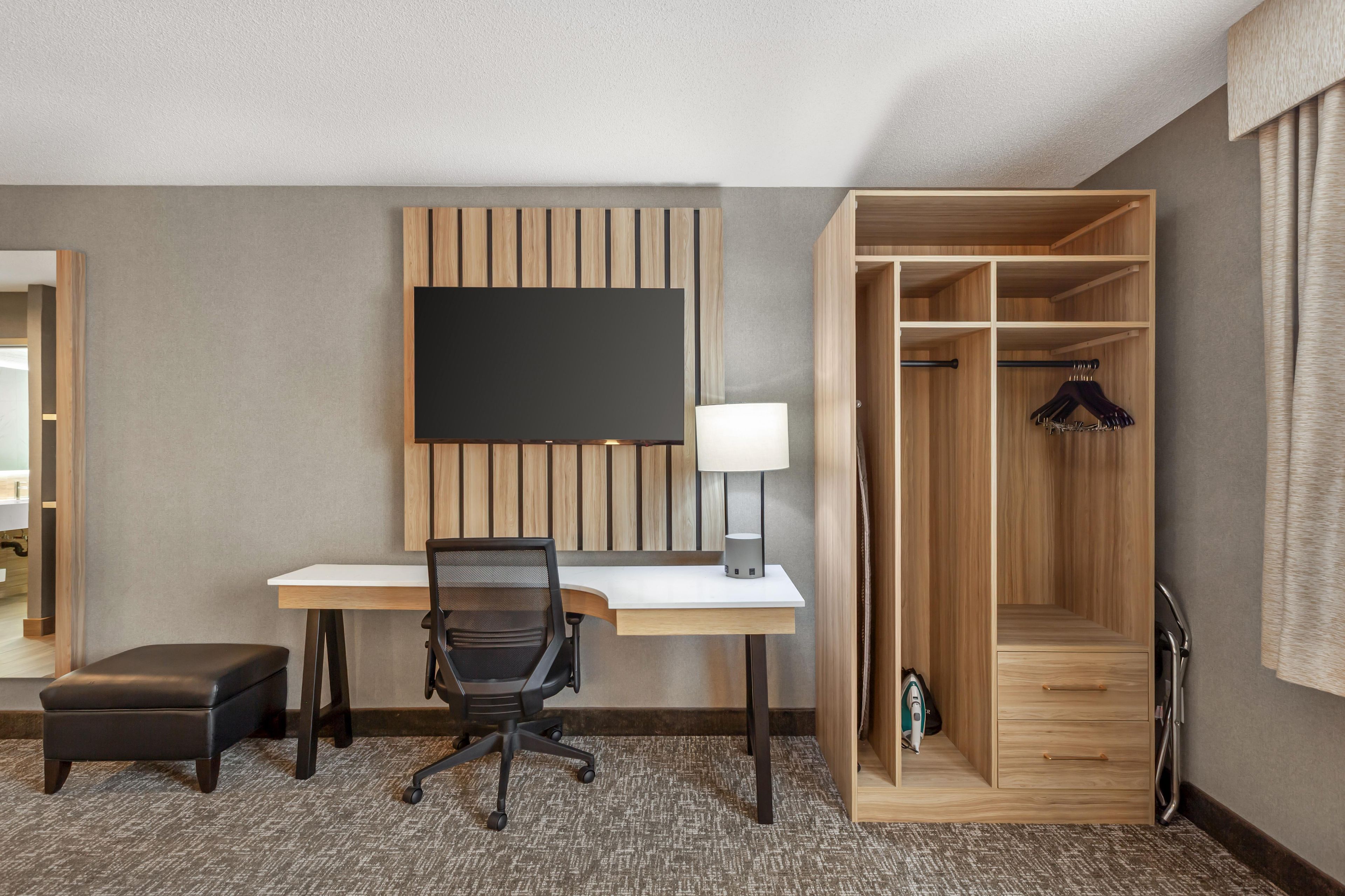 A hotel room with a desk, chair, and a wardrobe with hanging space.