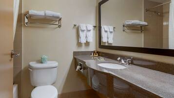 A bathroom with a toilet, sink, and mirror. There are towels on a rack and a shower curtain.