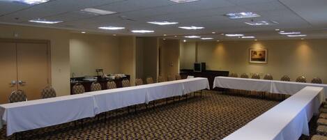 Un salón de conferencias con una larga mesa, sillas, piso alfombrado, luces en el techo y una puerta.