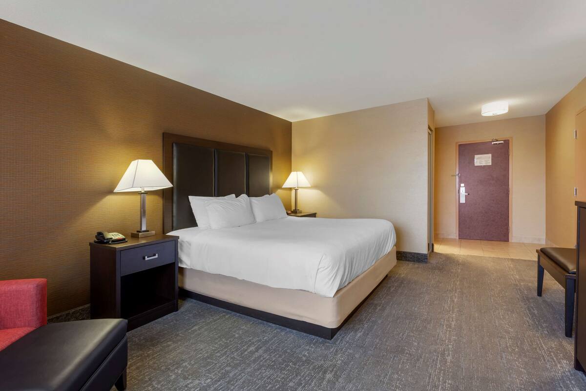 Une chambre d’hôtel avec un grand lit, deux tables de chevet avec des lampes, un fauteuil rouge et un banc en bois.