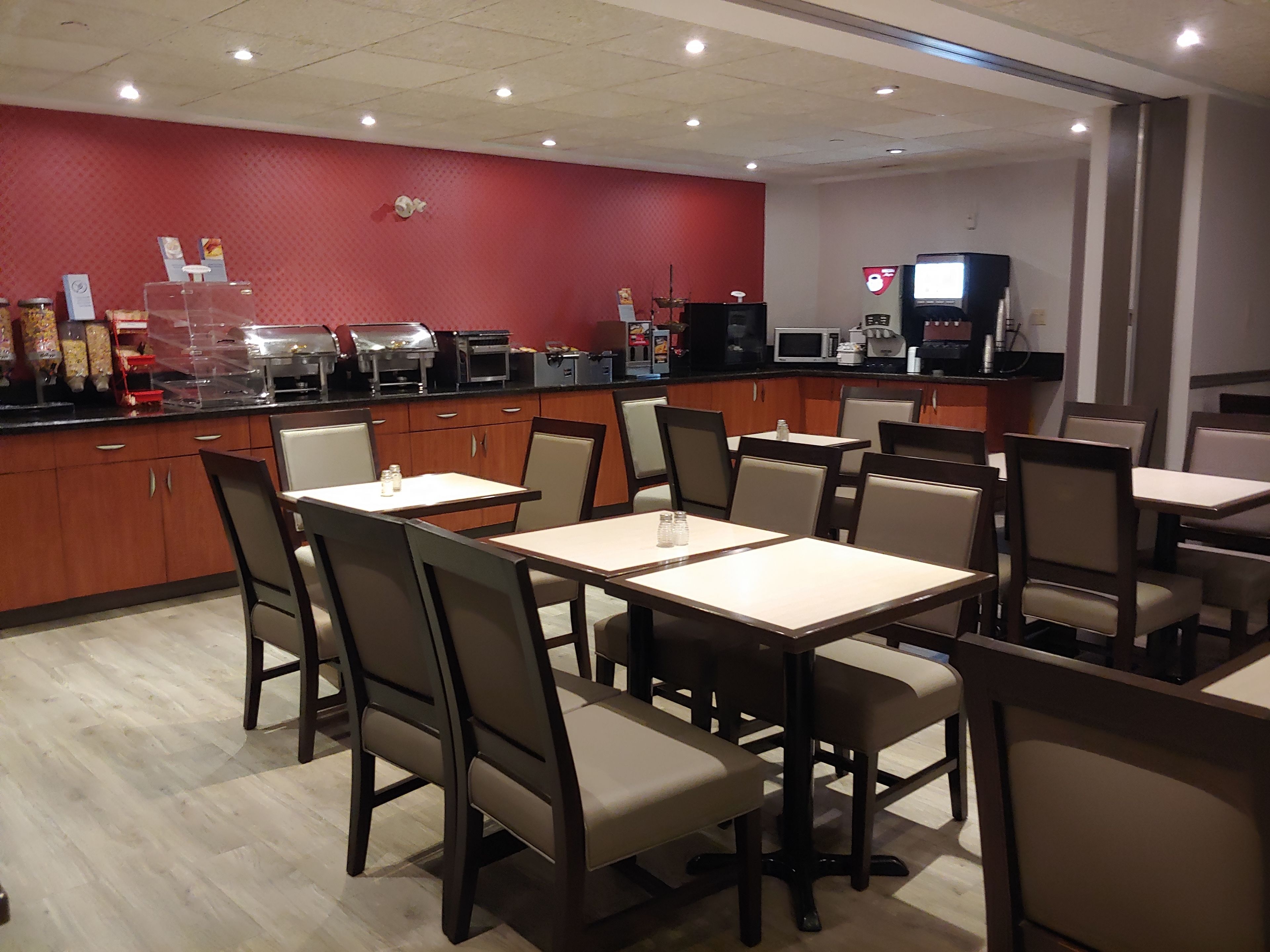 A restaurant with wooden cabinets, beige chairs, and a red wall.