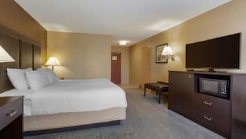 A hotel room with a bed, bedside table, lamp, TV, and a microwave in a cabinet.