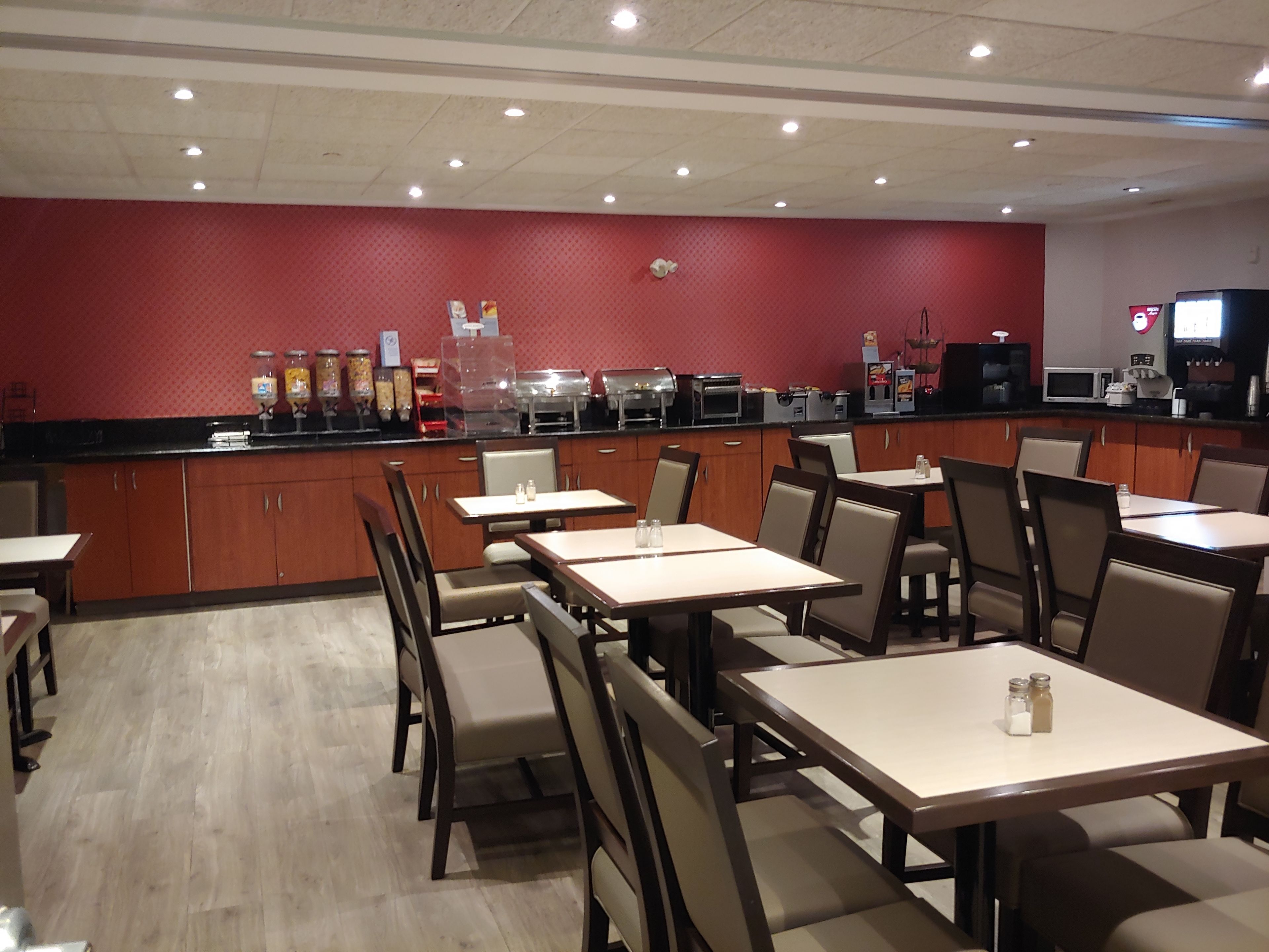 Un restaurante con varias mesas y sillas, una barra con dispensadores de comida y bebida, y un microondas.