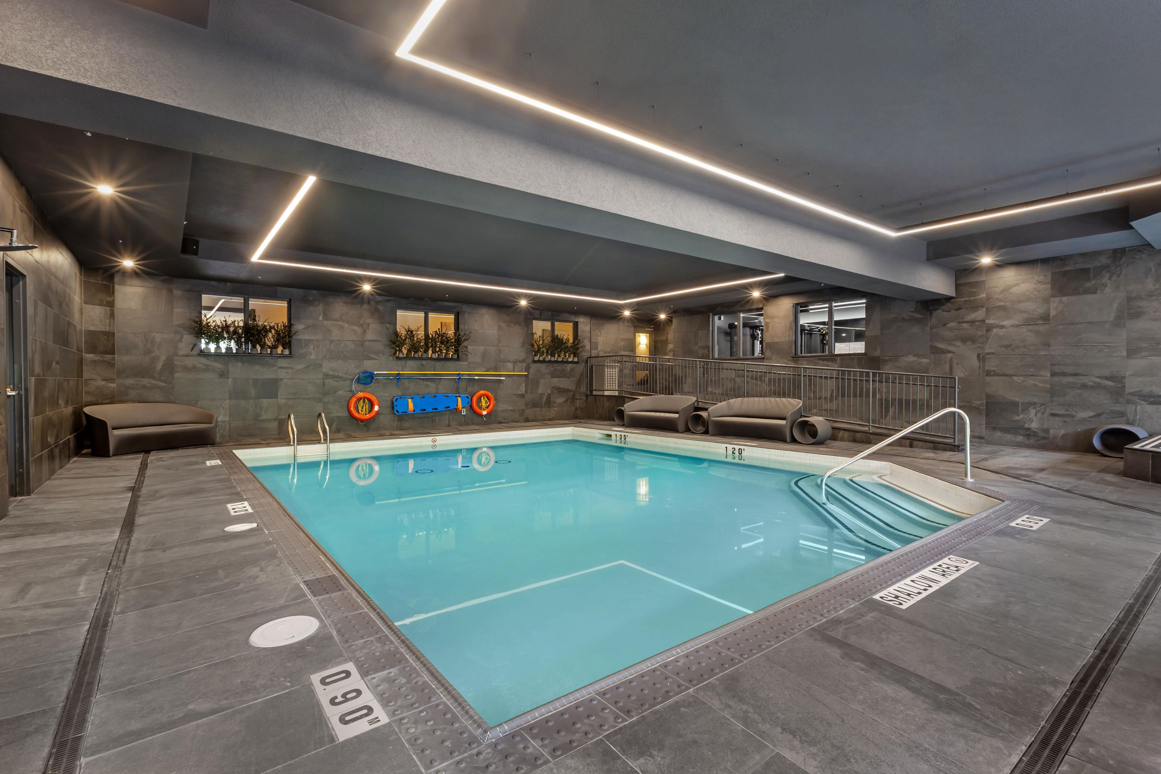 A modern indoor swimming pool with clear water, marked depth lines, and safety equipment.
