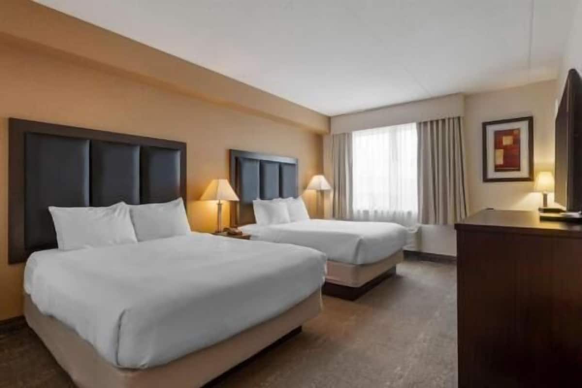 Une chambre d’hôtel avec deux lits, un bureau, une lampe et un tableau au mur.