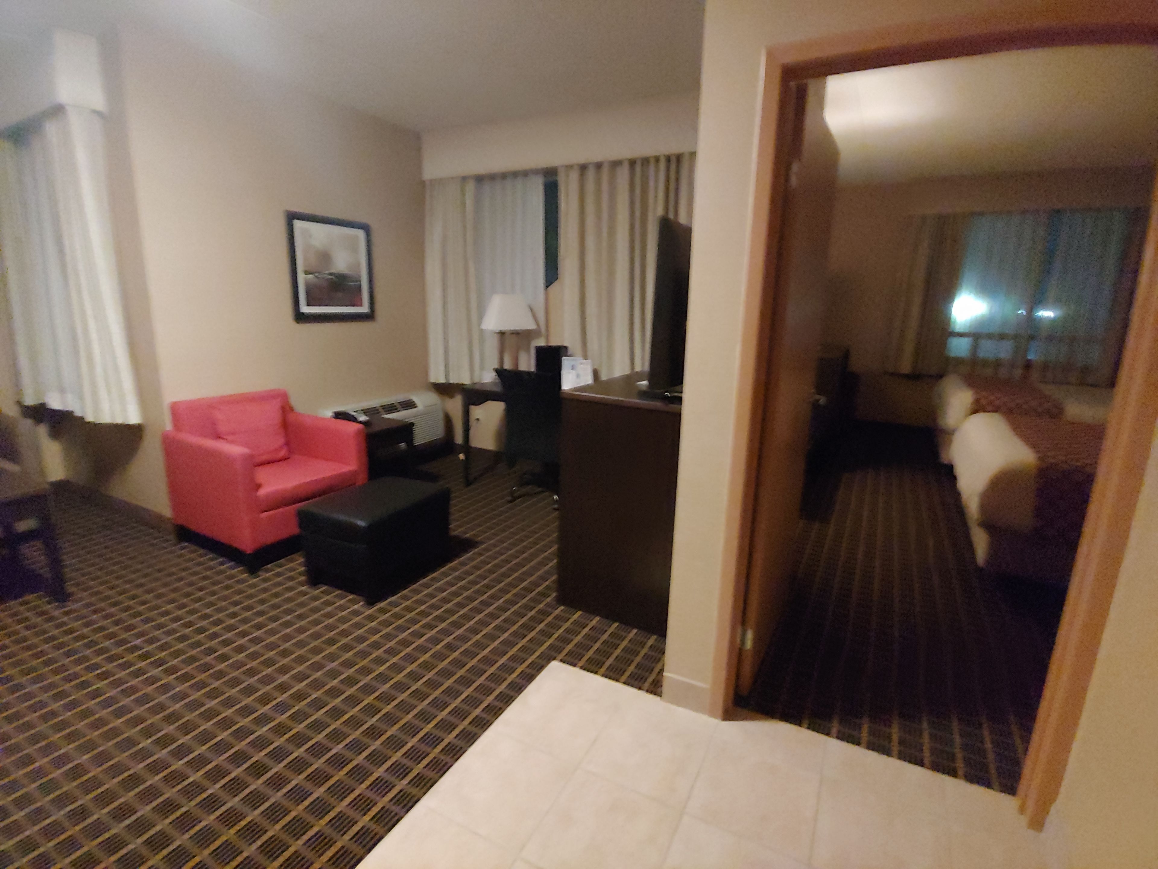 A hotel room with a red sofa, a desk with a lamp, a television, and a bed with a striped blanket.