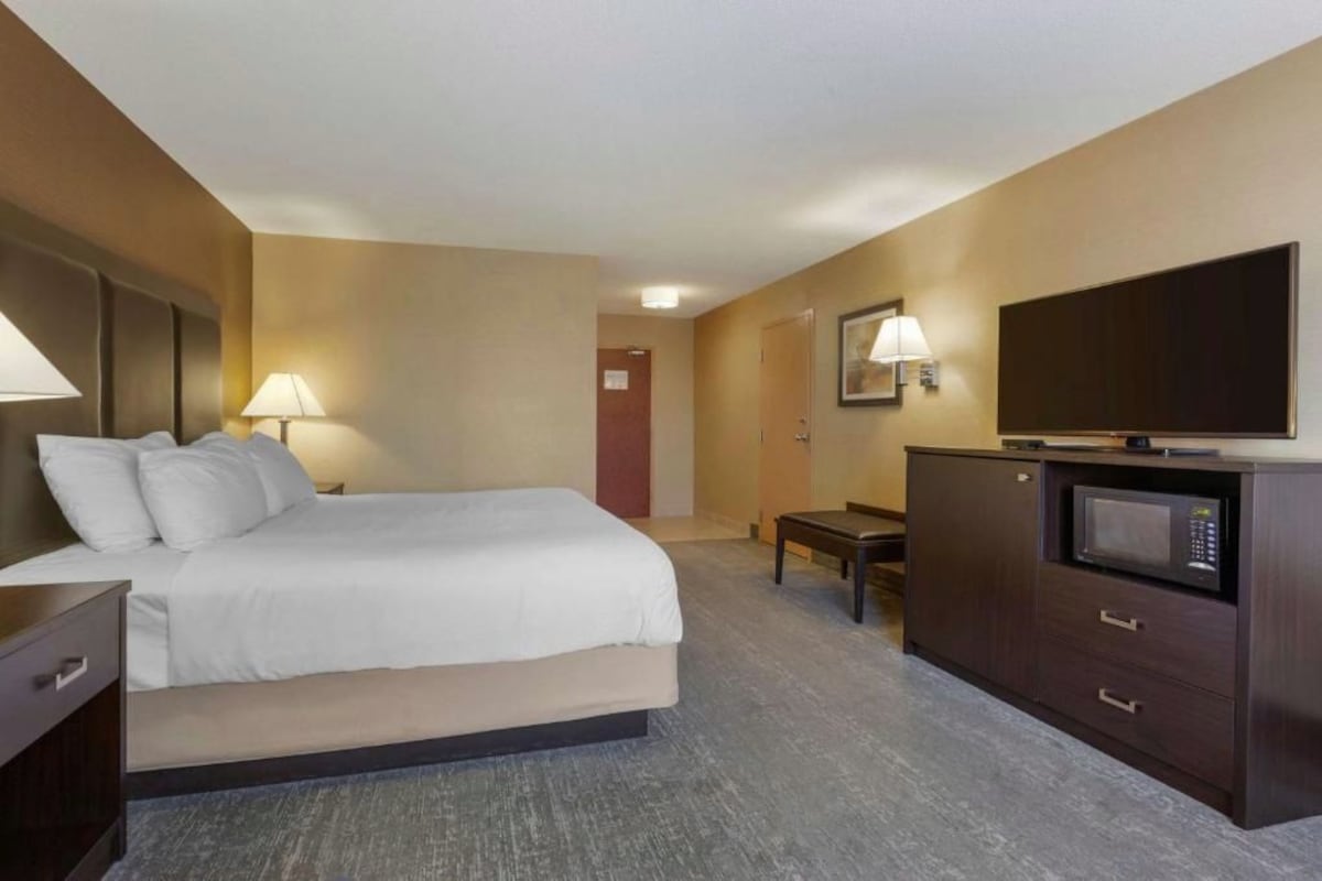 A hotel room with a bed, bedside table, lamp, TV, and a small desk with drawers.