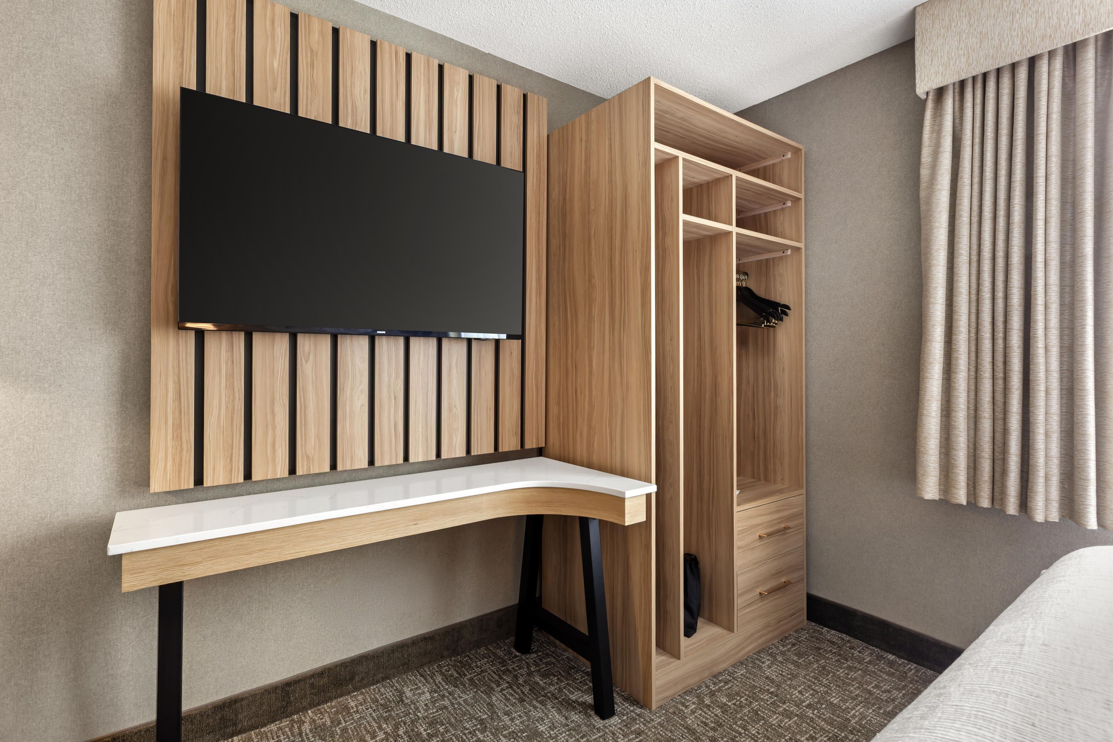 A hotel room with a built-in desk, a wardrobe with hanging space, and a bed.