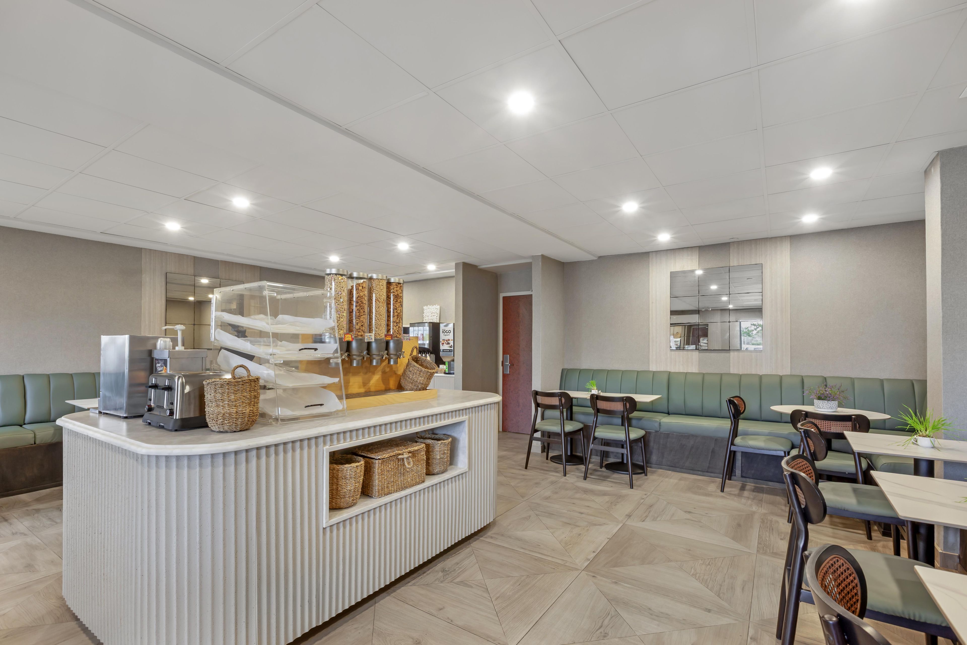 A modern cafe with a central counter, seating area, and a large mirror on the wall.