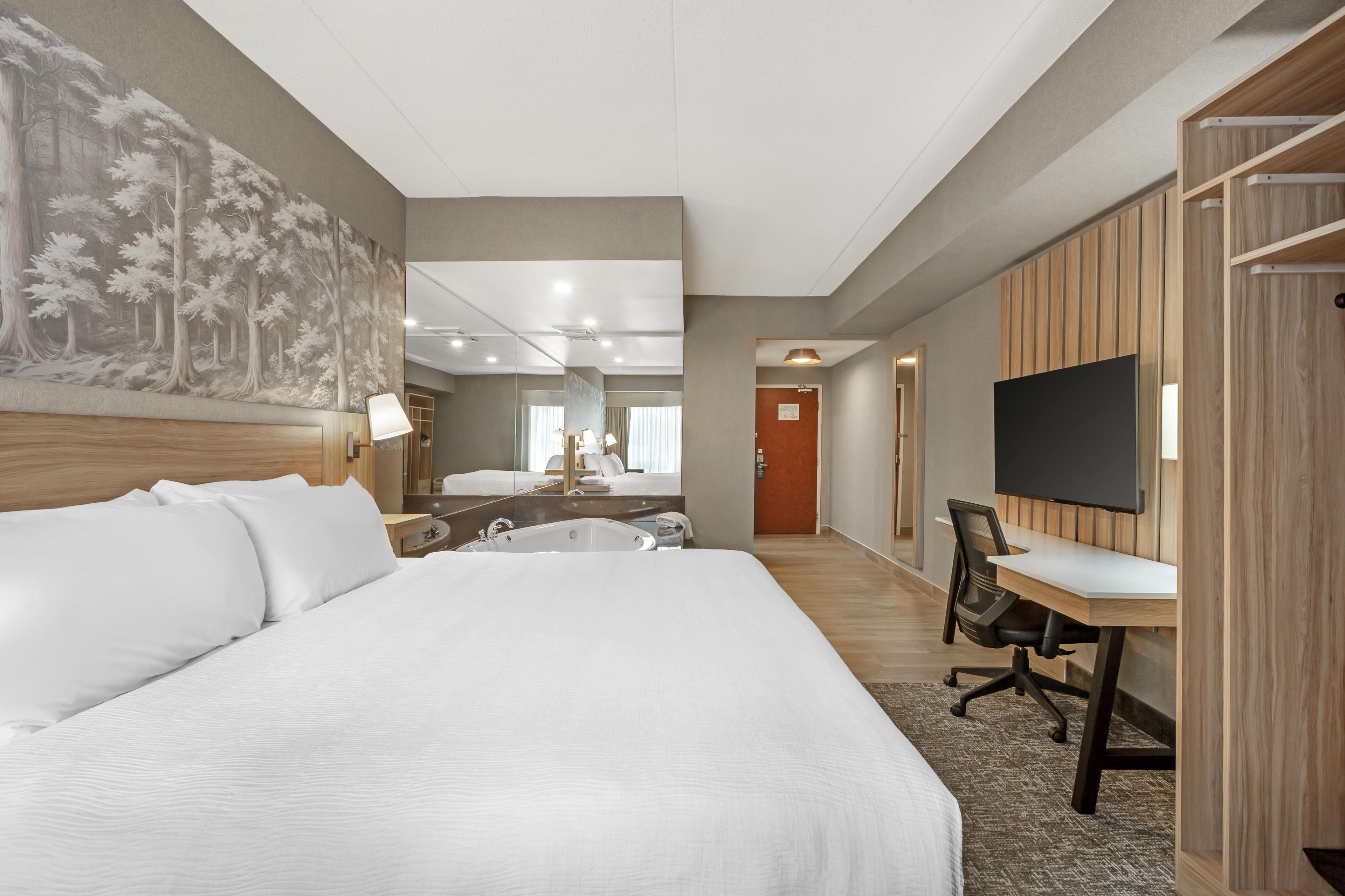 Habitación de hotel con una cama grande, un escritorio con silla, televisor y un baño con bañera.