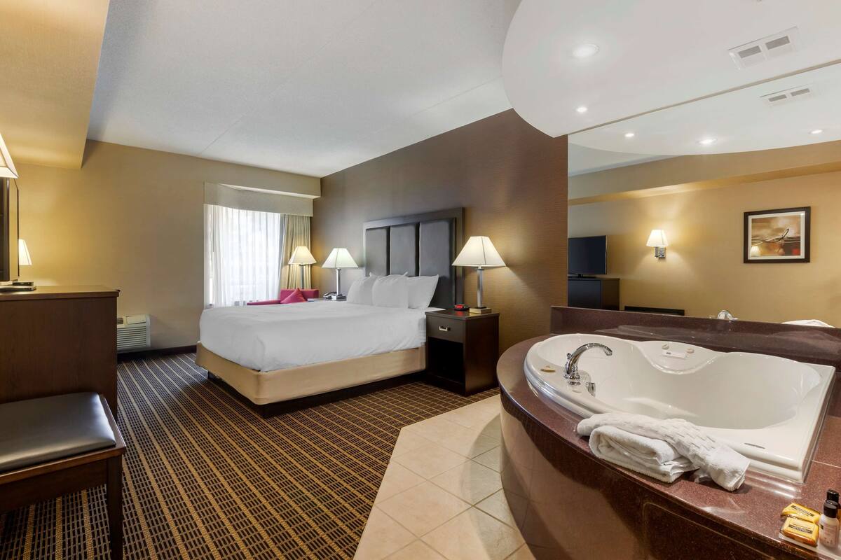 Une chambre d’hôtel avec un grand lit, une salle de bain séparée avec une baignoire et un bureau avec une chaise.
