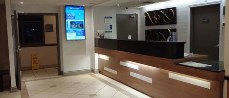 A reception area with a digital display, a reception desk, and a tiled floor.