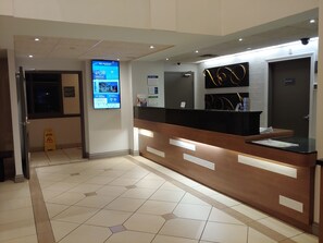 A reception area with a digital display, a reception desk, and a tiled floor.