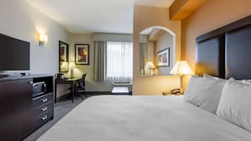 A hotel room with a large bed, a desk with a chair, a television, and a lamp.