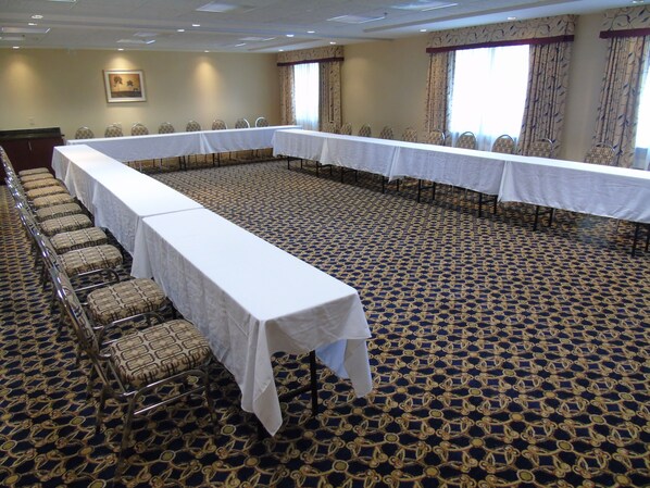 A conference room with a long table and chairs, carpeted floor, and windows with curtains.