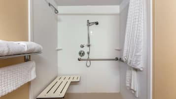 Pequeño espacio de ducha cerrado, de color blanco, con barra de apoyo, toallero y ducha.