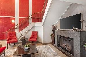 Una sala de estar moderna con chimenea, sillones tapizados en rojo, un televisor de pantalla plana y una escalera con paredes de diseño rojo.