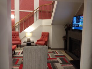 A living room with a fireplace, two armchairs, a small table with a lamp, and a TV mounted on the wall.