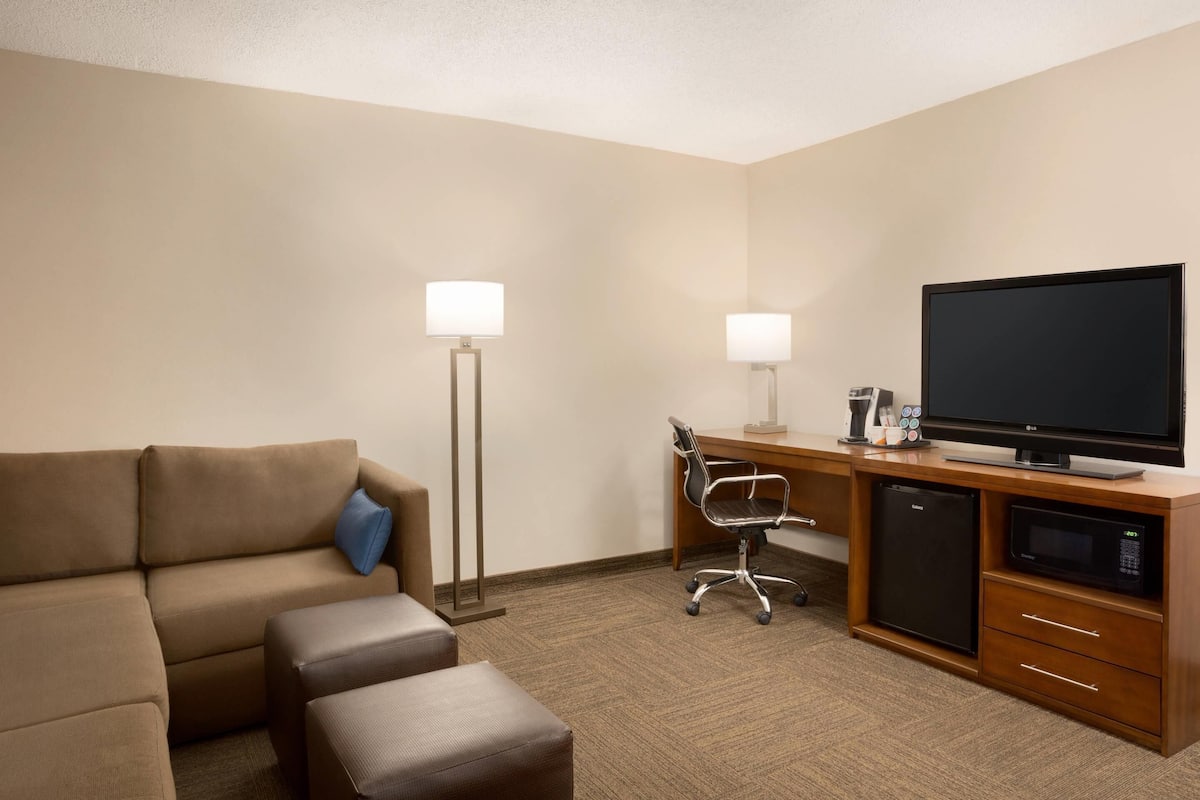 Una habitación de hotel con un sofá, un escritorio con ordenador, televisor y refrigerador.