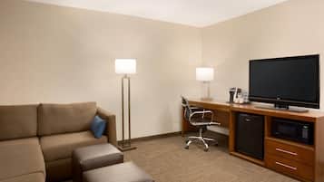 Una habitación de hotel con un sofá, un escritorio con ordenador, televisor y refrigerador.