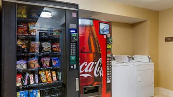 A vending machine with snacks and a Coca-Cola machine next to a laundry area.