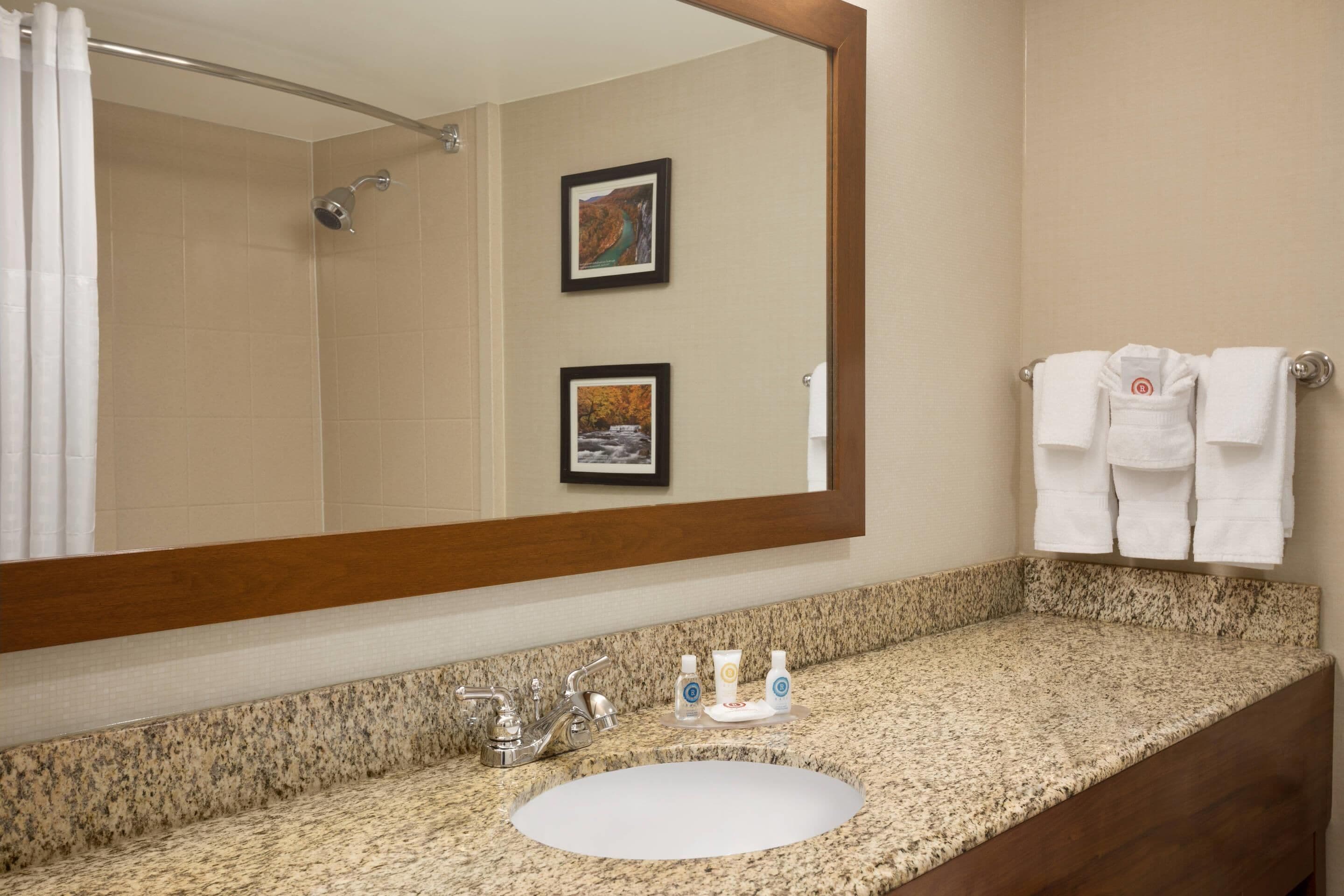 A bathroom with a granite countertop, a sink, a shower, and two framed pictures on the wall.