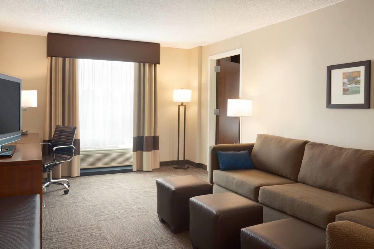 Una habitación de hotel con sofá, reposapiés, escritorio, silla y televisor.