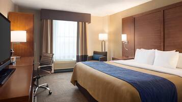 A hotel room with a large bed, a desk with a computer, a chair, and a TV.